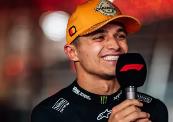 Lando Norris smiling with an F1 microphone and an orange championship cap.